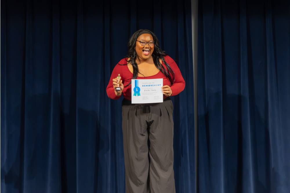 Reette Thorns smiling on stage with her 1st place award and certificate.